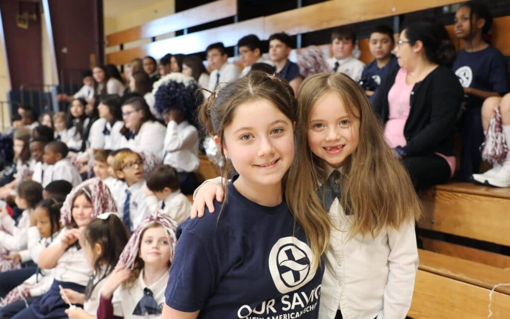 Two young girls smile for a photo in a gym during a game.