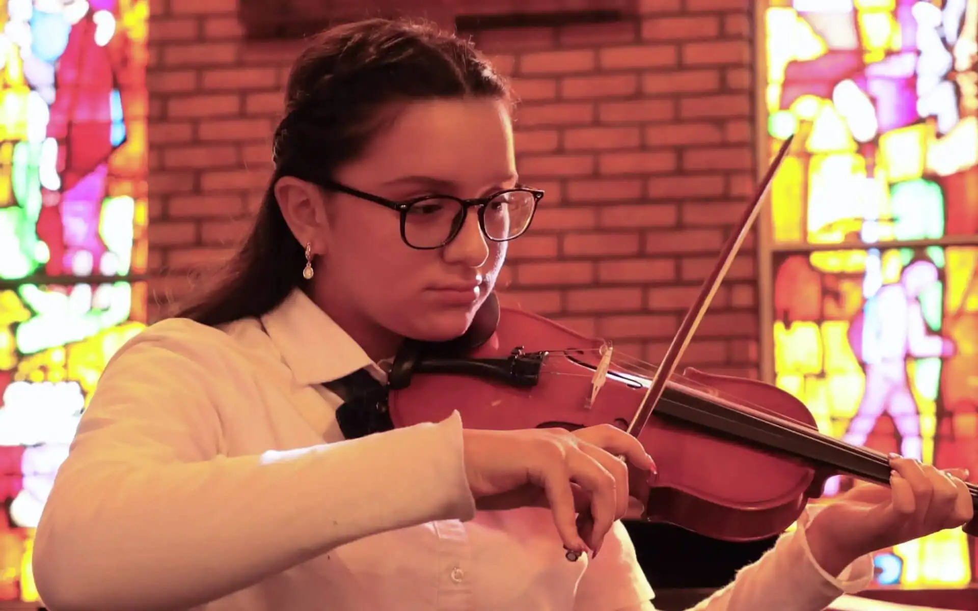 Female student plays violen against a backdrop of stained glass windows in a church.